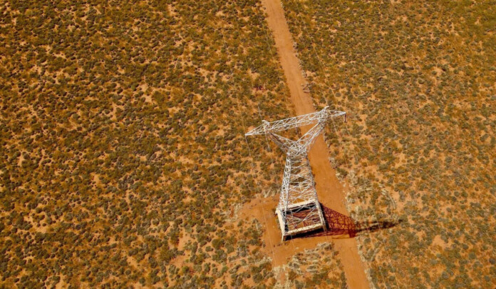 Lone transmission tower stands in red dirt in the Pilbara region