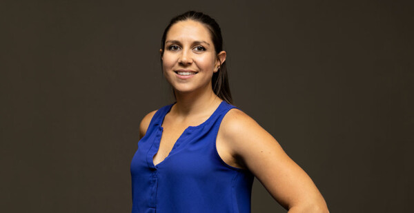 Young First Nations woman poses for photo wearing bright blue blouse against black background